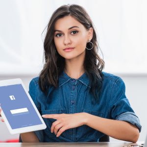 attractive young woman pointing on digital tablet screen with facebook website