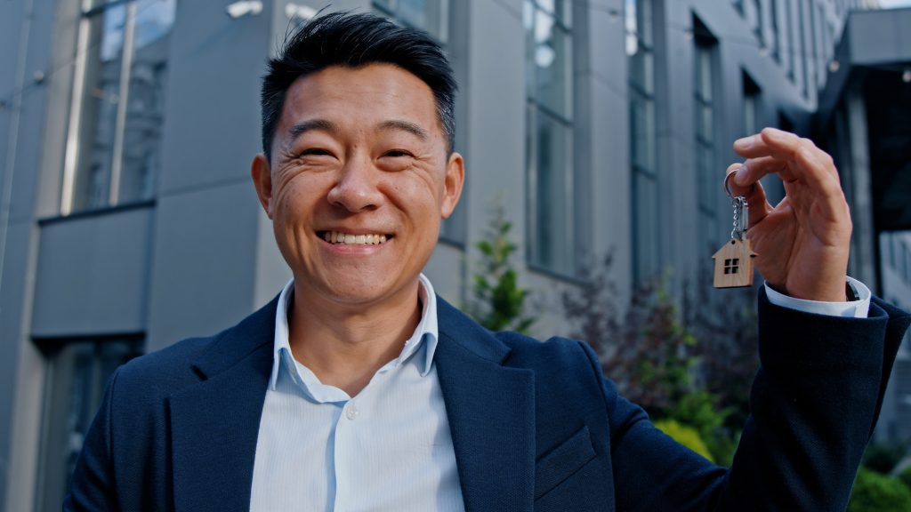 Happy smiling Asian adult 40s man holding keys portrait outdoors win reaction victory celebrate male