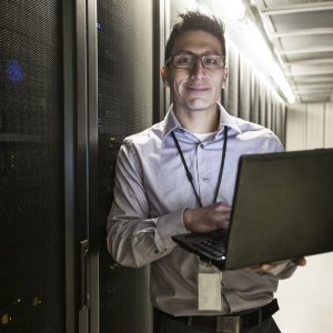 Hispanic man technician doing diagnostic tests on computer servers in a large server farm.