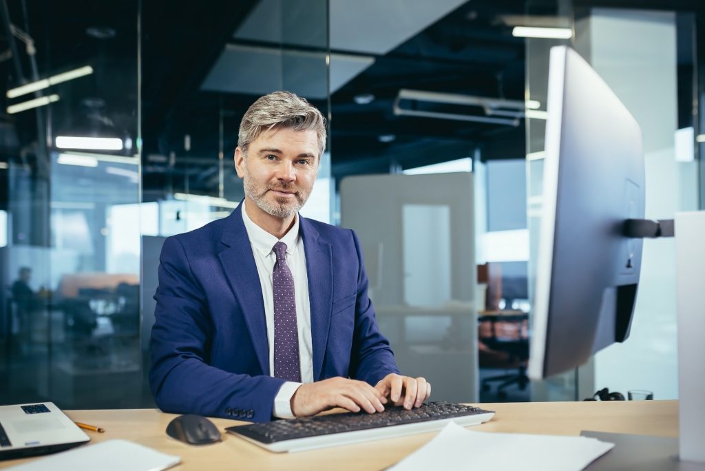 Portrait of a successful gray-haired man with a beard, businessman working at a computer