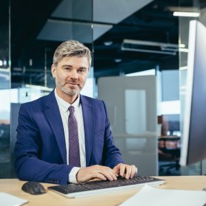 Portrait of a successful gray-haired man with a beard, businessman working at a computer