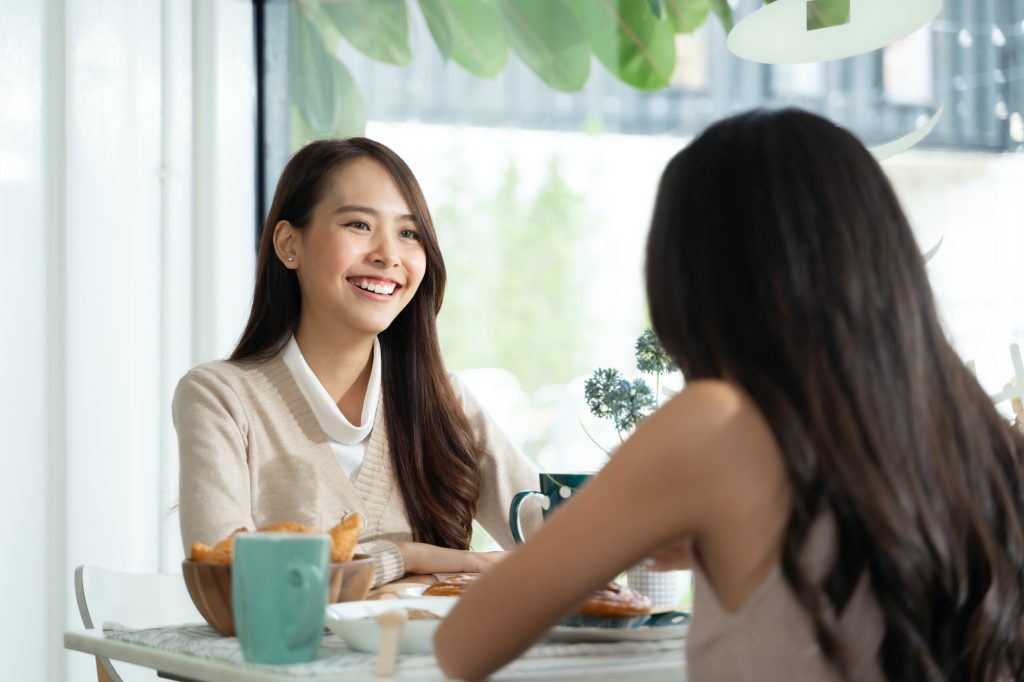 Two young Asian women friends talking at a coffee shop