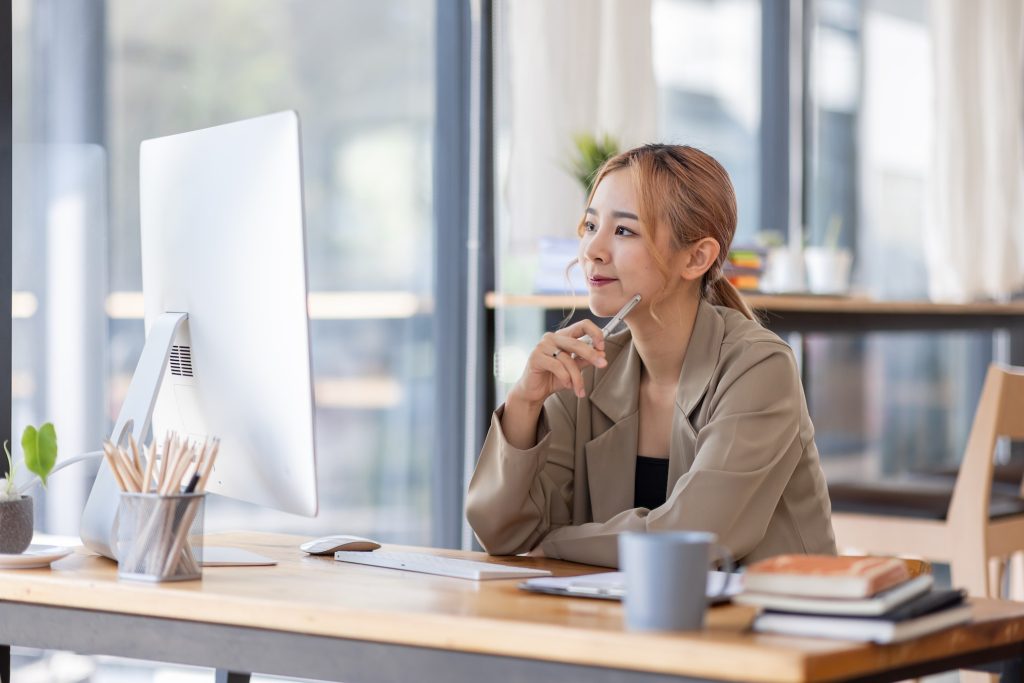 Young Asian professional business woman office worker analyst sitting at desk working on laptop thin
